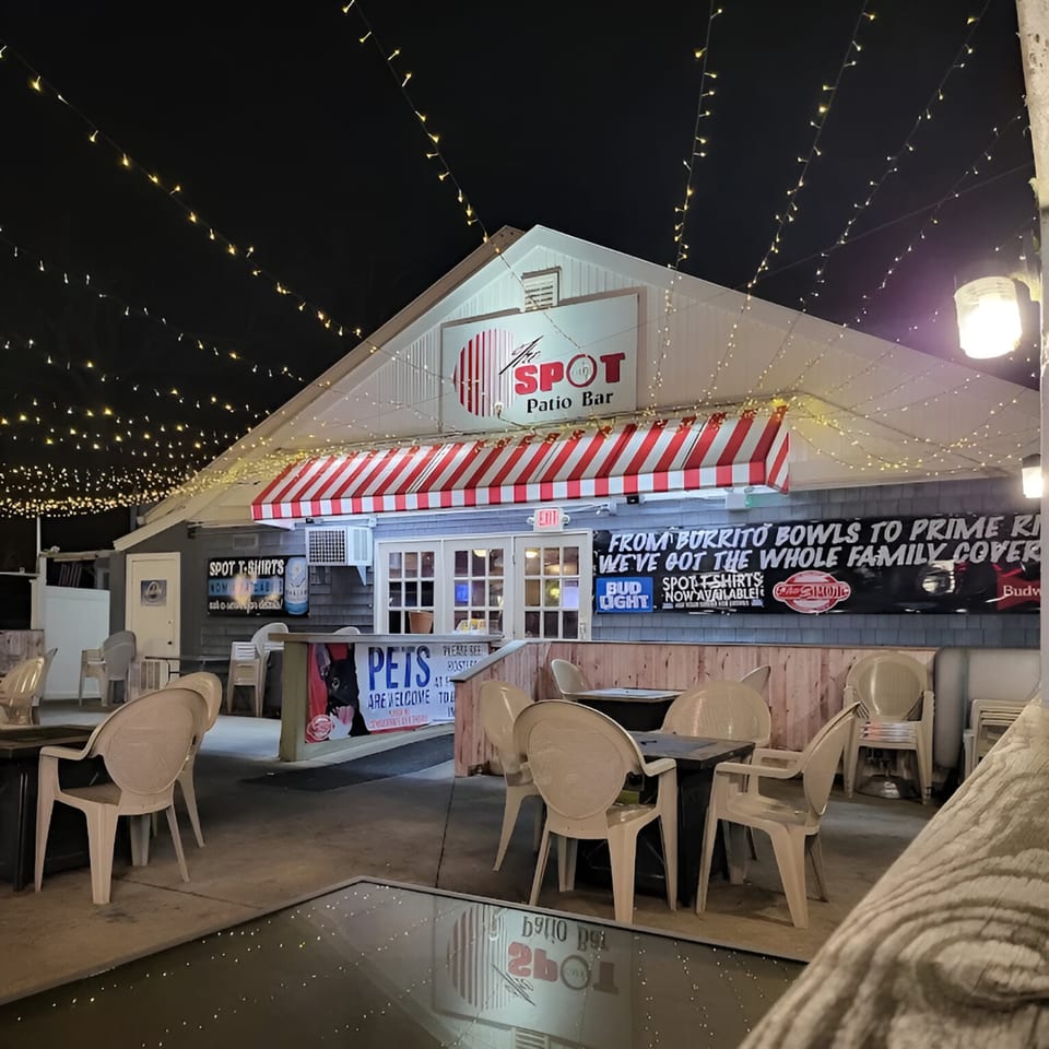 The Spot Cafe patio at night, illuminated by string lights and a red and white striped awning.