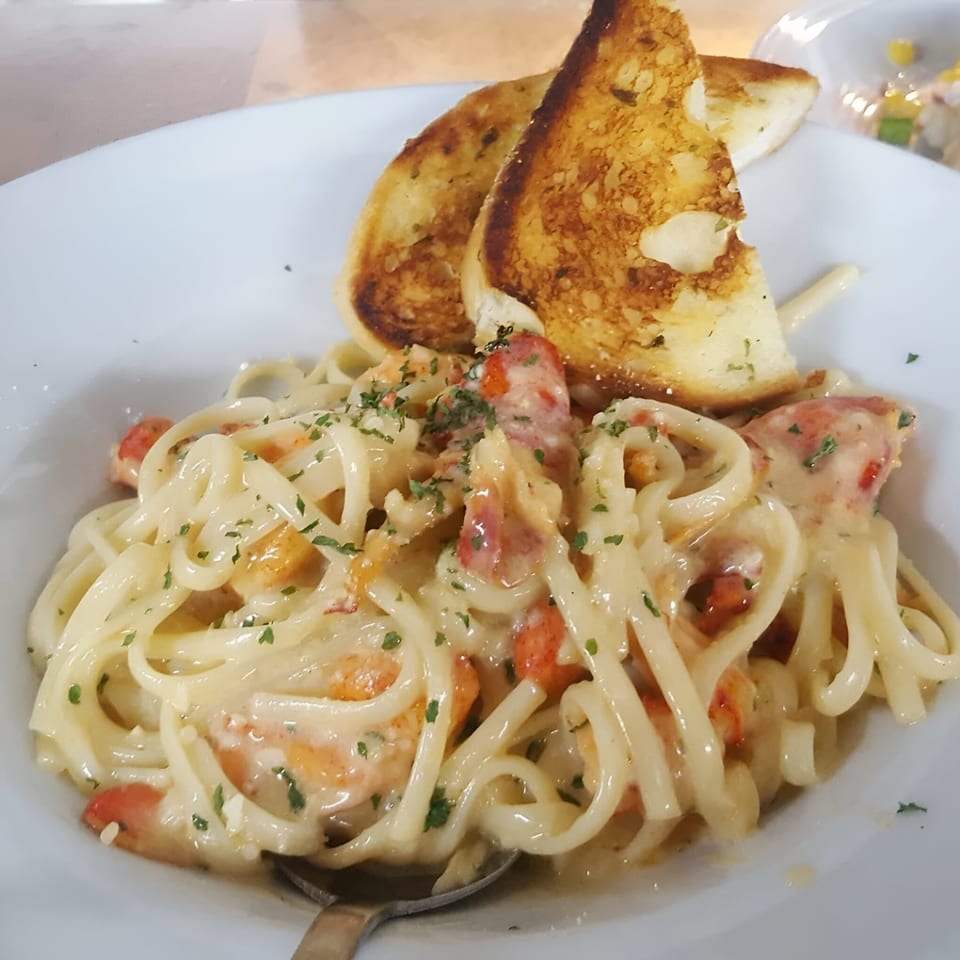 Creamy linguine pasta with red sauce, shrimp, and two slices of garlic bread on a white plate.