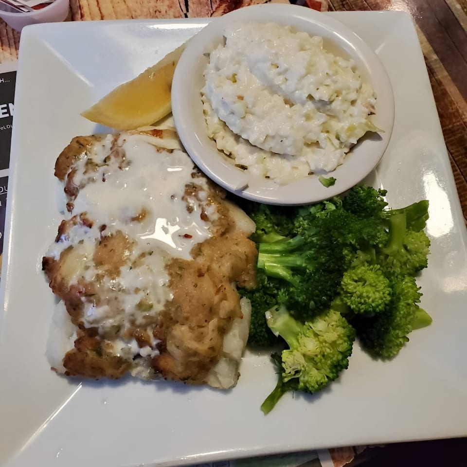A white plate with crab-stuffed fish, a side of rice, steamed broccoli, and a lemon wedge.