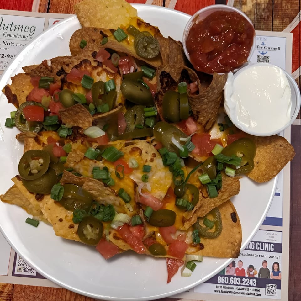 A plate of The Spot Cafe's nachos with melted cheese, jalapenos, tomatoes, and green onions, served with salsa and sour cream.