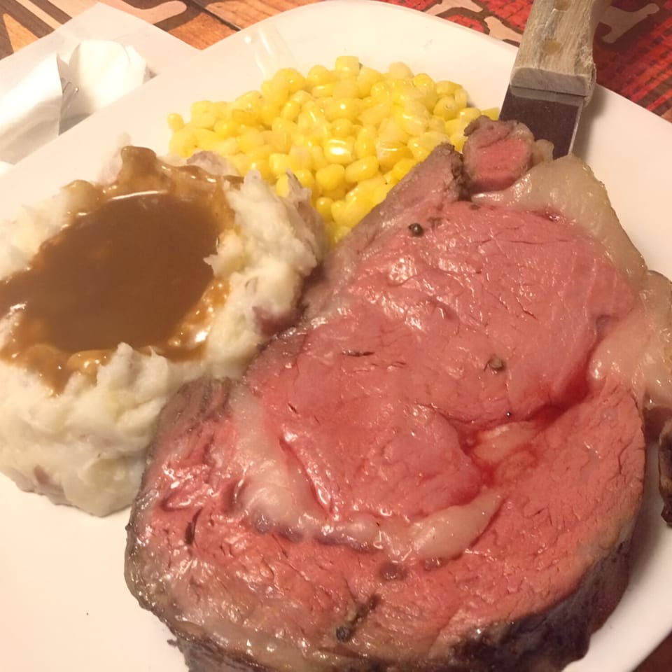 A prime rib dinner with mashed potatoes and gravy, corn, and a steak knife on a white plate.