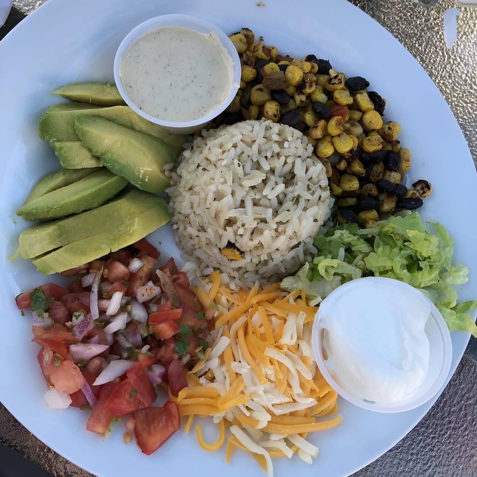 A colorful plate from The Spot Cafe with rice, avocado, corn, beans, salsa, shredded cheese, and sour cream.