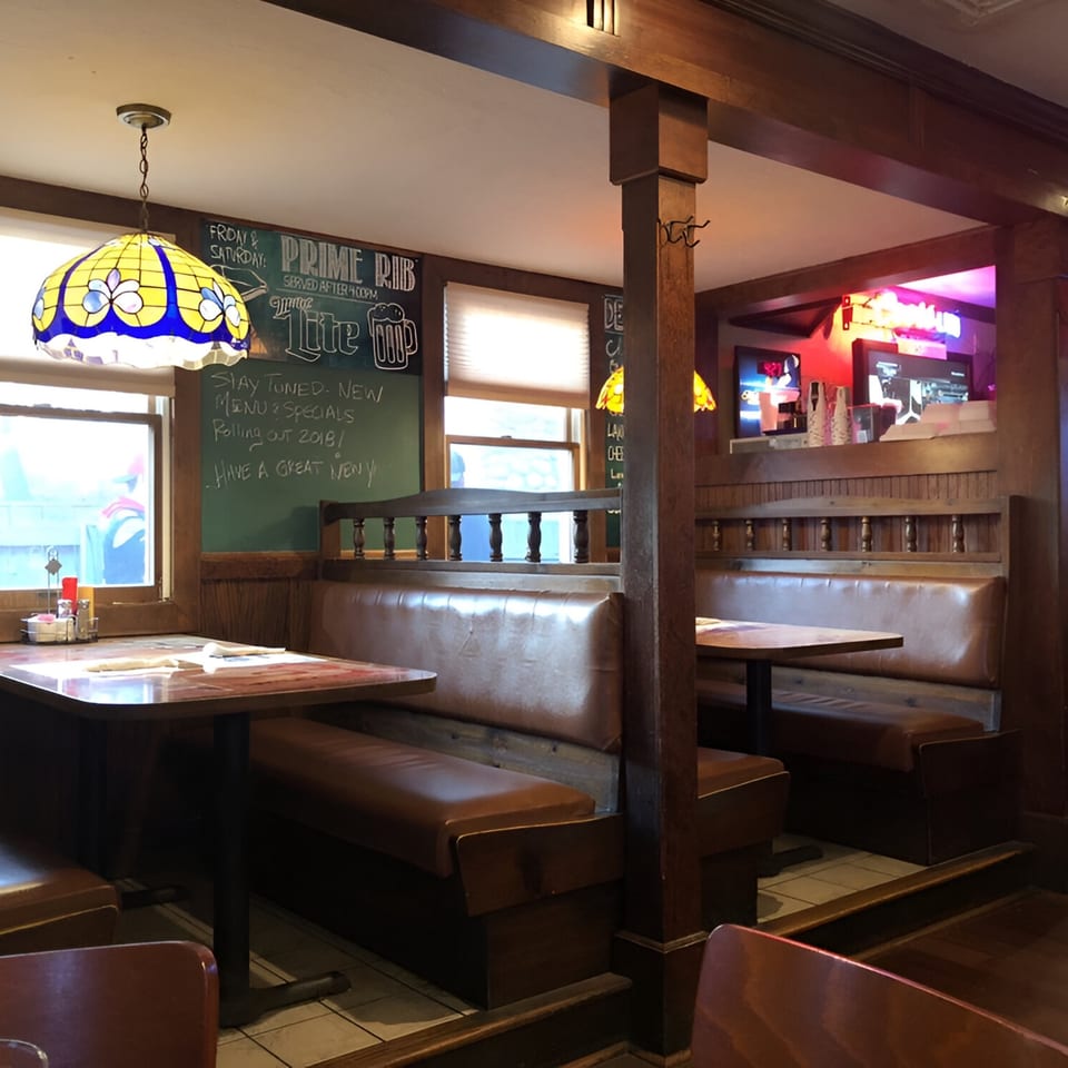 Cozy interior of The Spot Cafe with wooden booths, tables, and a stained-glass lamp, featuring a chalkboard menu.